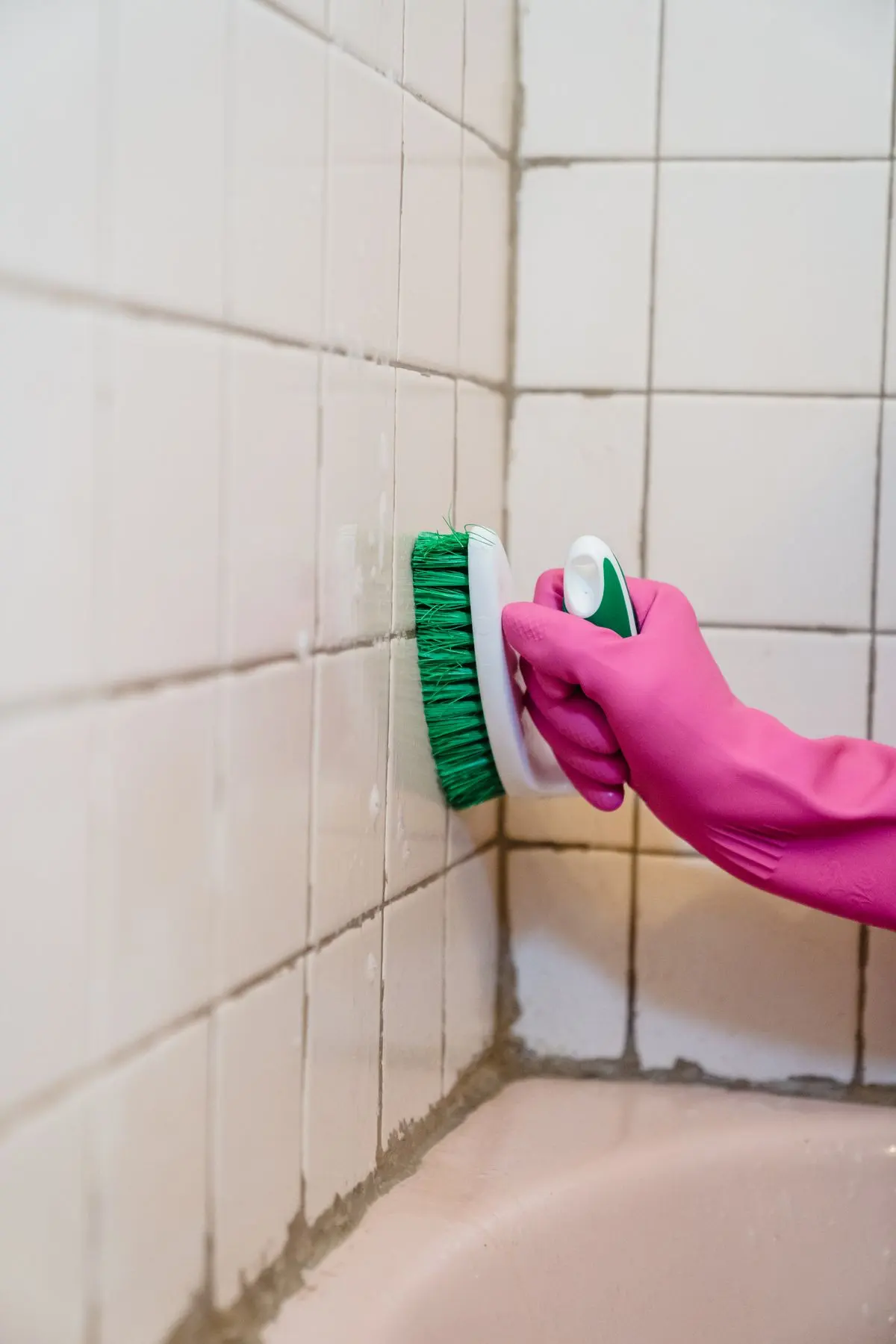 Gloved hand scrubbing bathroom tiles and grout