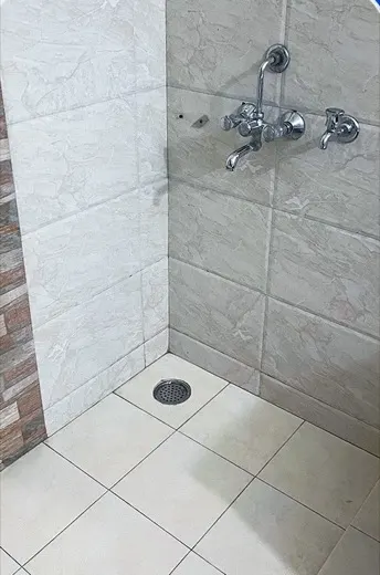 Bathroom shower area with heavy hard-water scale and staining on the tiles and floor before cleaning, and the same shower area with the tiles and floor restored to clean