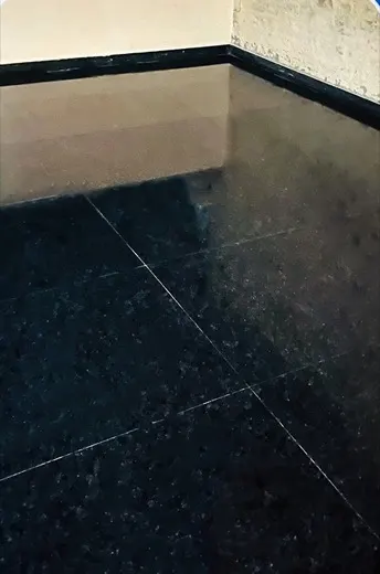 Dark stone floor covered in a pale film of grime and staining before cleaning, and the same floor restored to a deep even finish